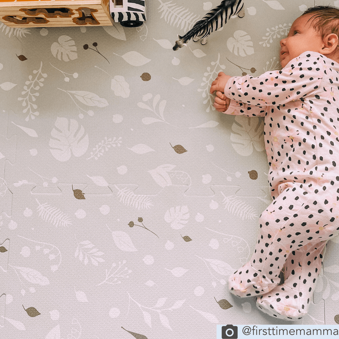 baby playing on the Metallic Garden playmat, features a charming design of white leaves on a stylish grey background with pops of metallic gold.