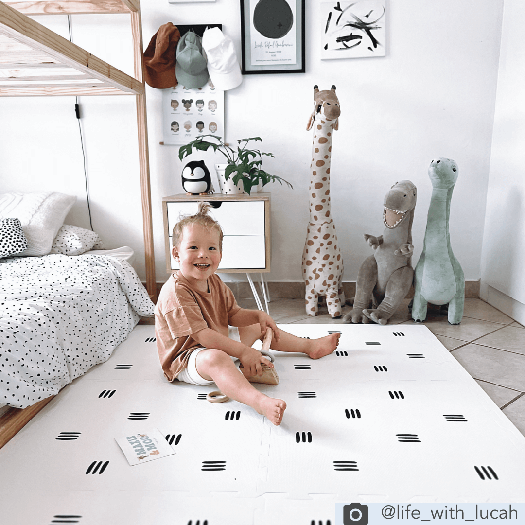 The White with black stripes play mat from Maxie and Moo, set up in a child’s room, with a child having fun playing on the play mat made of thick, soft, padded EVA foam.
