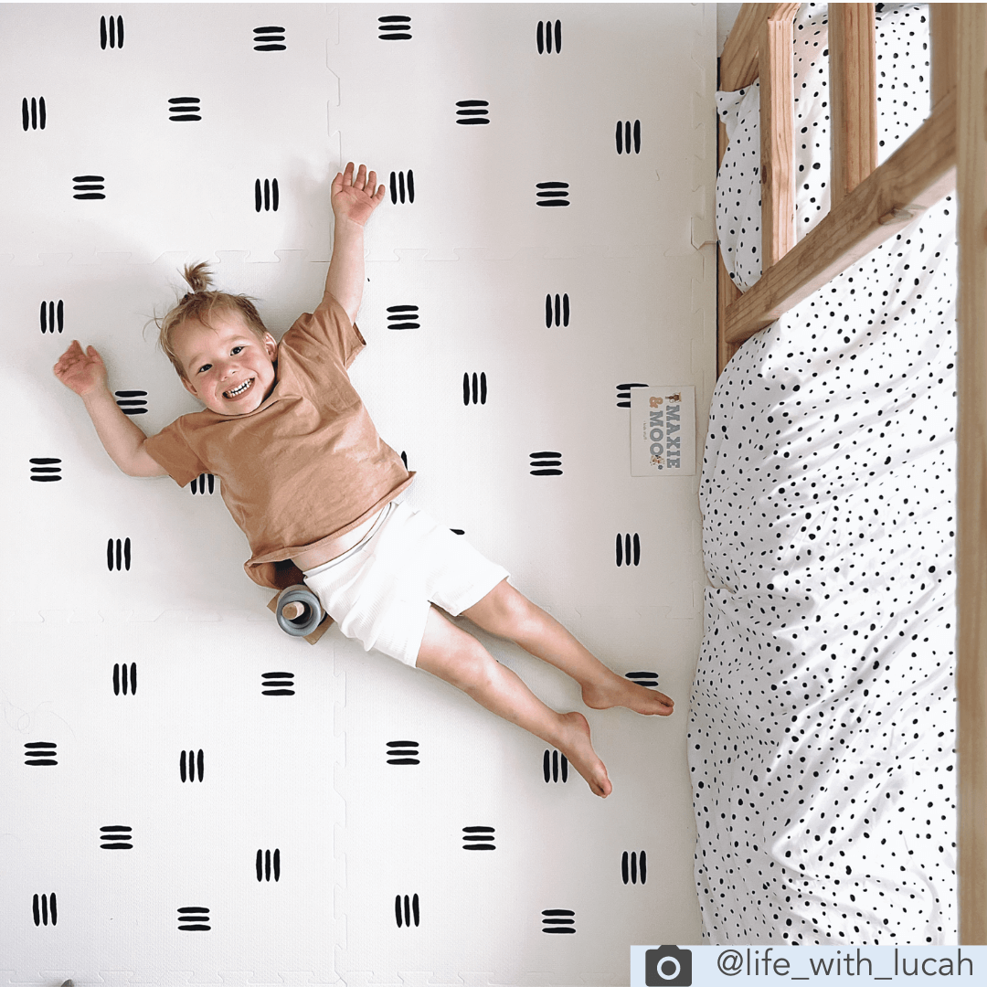 Child lying on the White with black stripes play mat from the Maxie and Moo Luxury collection. This play mat features a sleek and modern monochrome design of white mat with 3 black stripes.