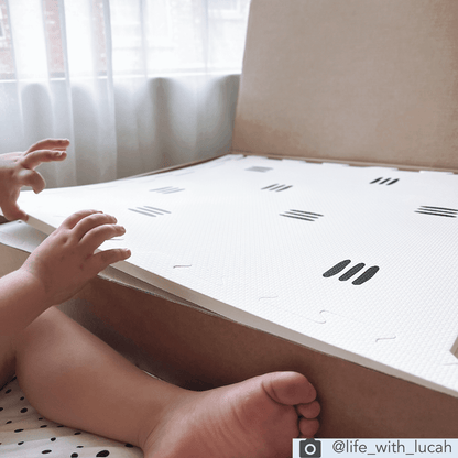 This image showcases the White with black stripes play mat, as it is unboxed by a child. This play mat features a sleek and modern monochrome design of white mat with 3 black stripes. The unique and timeless design of this play mat adds a touch of class and sophistication to any play area or nursery.