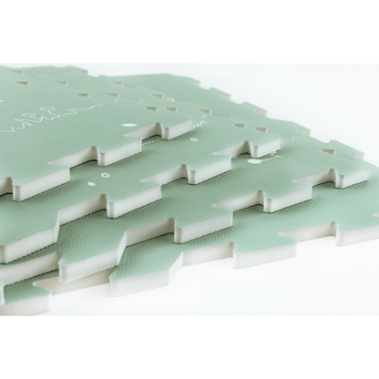 Stacked playmat tiles from the Fairytale Forest Mint Green Play Mat. Showcasing pour premium playmat's thickness and high-quality construction. The play mat features a scenic forest design with trees, flowers, and animals, creating a durable and comfortable play space for children.